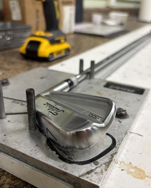 A Titleist iron clamped in a repair jig on the shop bench